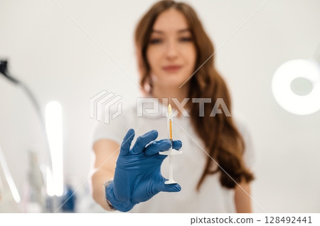 Close up view. Cosmetologist holding syringe for injection lips augmentation. Women's cosmetology in the beauty salon Close up view. Cosmetologist holding syringe for injection lips augmentation. Women's cosmetology in the beauty salon 128492441