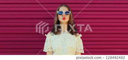 Beautiful young woman blowing a kiss with red lipstick, model posing on pink background 128492482