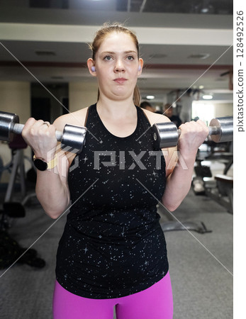 Ordinary woman in the gym doing exercises with dumbbells. Workout for weight loss. Body strengthening and healthy lifestyle Ordinary woman in the gym doing exercises with dumbbells. Workout for weight loss. Body strengthening and healthy lifestyle 128492526
