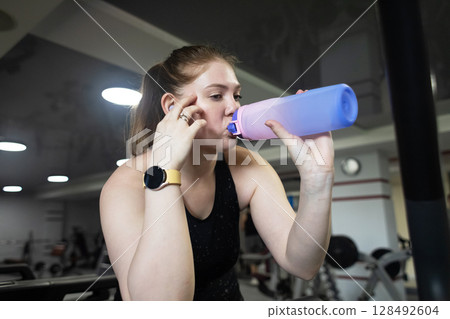 Woman tired from running on treadmill and drinking water from bottle. Complex cardio workout and rest from exercises in gym Woman tired from running on treadmill and drinking water from bottle. Complex cardio workout and rest from exercises in gym 128492604