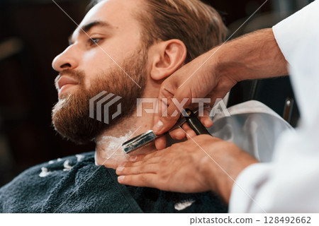 Getting shaved. Man is visiting modern barber shop. Modern style 128492662