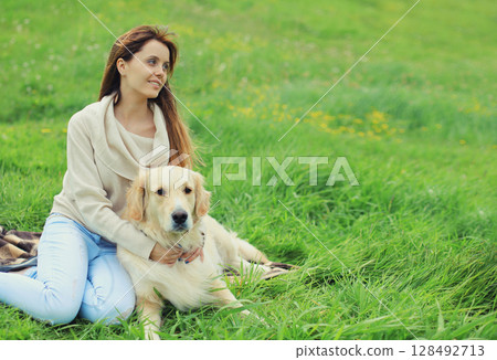Happy owner young woman with Golden Retriever dog sitting on grass together in summer park 128492713