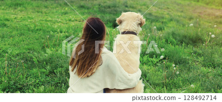 Happy owner young woman with Golden Retriever dog sitting on grass together in summer park 128492714