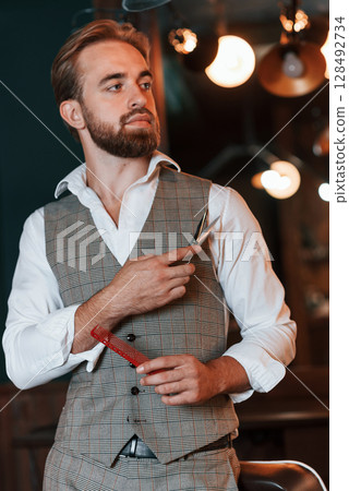 Standing, holding equipment. Handsome barber is in the salon 128492734