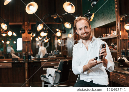 Hair clipper is in hand. Handsome barber is in the salon Hair clipper is in hand. Handsome barber is in the salon 128492741