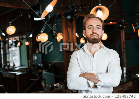 Standing with arms crossed. Handsome barber is in the salon 128492748