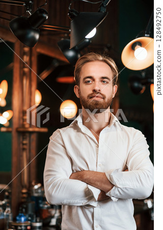 Standing with arms crossed. Handsome barber is in the salon 128492750