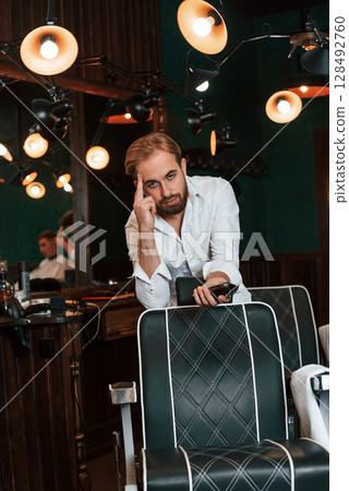 Leaning on the chair. Handsome barber is in the salon 128492760
