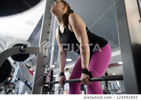 Plus size woman doing exercises on Smith Machine. Squats on a simulator with a barbell. Workout for weight loss 128492893