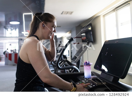 Real woman with a normal body working out on treadmill in gym. Realistic fitness and healthy weight loss motivation Real woman with a normal body working out on treadmill in gym. Realistic fitness and healthy weight loss motivation 128492924