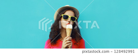 Summer portrait of happy young woman eating ice cream in hat and glasses on blue background Summer portrait of happy young woman eating ice cream in hat and glasses on blue background 128492991