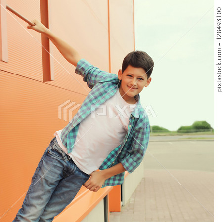 Happy smiling teenager boy in casual clothing in the city, orange wall background Happy smiling teenager boy in casual clothing in the city, orange wall background 128493100