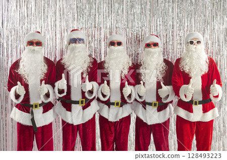 Happy funny people in Santa Claus costumes showing thumb up sign celebrating New Year and Christmas Happy funny people in Santa Claus costumes showing thumb up sign celebrating New Year and Christmas 128493223