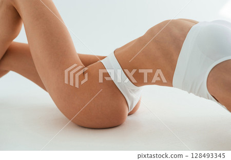Close up view of belly, on the floor. Young woman with slim body type is in fitness clothes in the studio Close up view of belly, on the floor. Young woman with slim body type is in fitness clothes in the studio 128493345