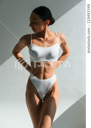 Shadow is on the body. Young woman in fitness clothes is in the studio Shadow is on the body. Young woman in fitness clothes is in the studio 128493349