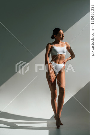 Shadow is on the body. Young woman in fitness clothes is in the studio Shadow is on the body. Young woman in fitness clothes is in the studio 128493352