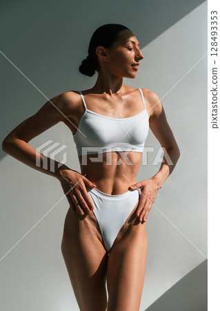 Showing abs. Young woman with slim body type is in fitness clothes in the studio Showing abs. Young woman with slim body type is in fitness clothes in the studio 128493353
