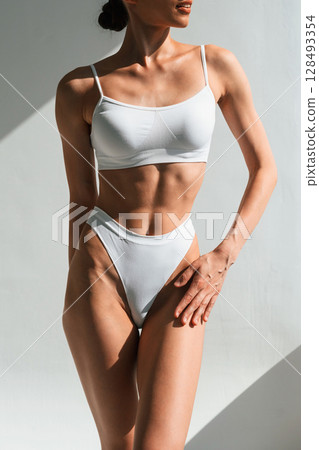 Showing abs. Young woman with slim body type is in fitness clothes in the studio 128493354