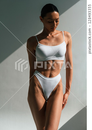Showing abs. Young woman with slim body type is in fitness clothes in the studio 128493355