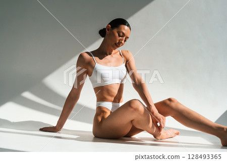 Daytime sunlight. Young woman with slim body type is in fitness clothes in the studio Daytime sunlight. Young woman with slim body type is in fitness clothes in the studio 128493365