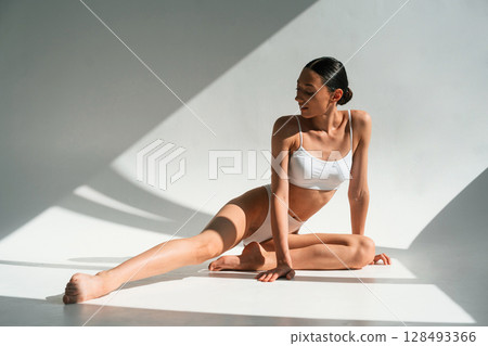 Daytime sunlight. Young woman with slim body type is in fitness clothes in the studio Daytime sunlight. Young woman with slim body type is in fitness clothes in the studio 128493366
