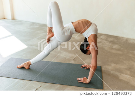 Spine exercises. Young woman with slim body type is in fitness clothes in the studio Spine exercises. Young woman with slim body type is in fitness clothes in the studio 128493373