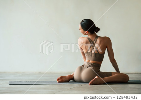 Flexible body, sitting, rear view. Young woman with slim body type is in fitness clothes in the studio Flexible body, sitting, rear view. Young woman with slim body type is in fitness clothes in the studio 128493432