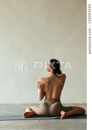 Flexible body, sitting, rear view. Young woman with slim body type is in fitness clothes in the studio 128493434