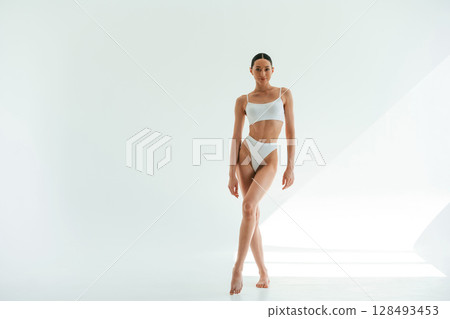 Standing and posing. Young woman with slim body type is in fitness clothes in the studio Standing and posing. Young woman with slim body type is in fitness clothes in the studio 128493453