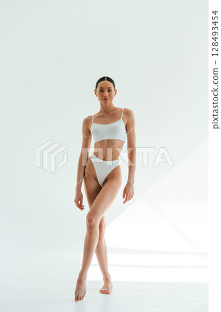 Standing and posing. Young woman with slim body type is in fitness clothes in the studio 128493454