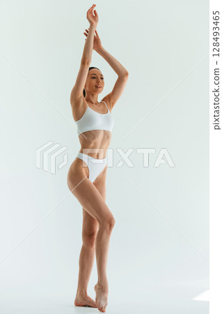 With hands up. Young woman with slim body type is in fitness clothes in the studio With hands up. Young woman with slim body type is in fitness clothes in the studio 128493465