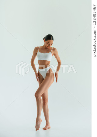 Against white background. Young woman with slim body type is in fitness clothes in the studio 128493467