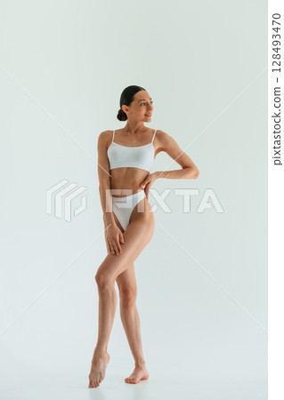 In white fitness clothes. Young woman with slim body type is in the studio 128493470