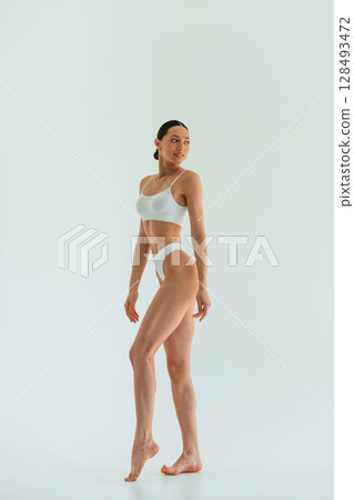 In white fitness clothes. Young woman with slim body type is in the studio 128493472