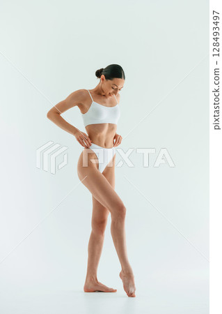 In the studio with white background. Young woman with slim body type is in fitness clothes In the studio with white background. Young woman with slim body type is in fitness clothes 128493497
