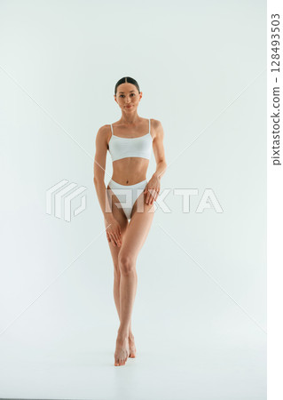 In the studio with white background. Young woman with slim body type is in fitness clothes In the studio with white background. Young woman with slim body type is in fitness clothes 128493503