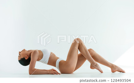 View from the side, on the floor. Young woman with slim body type is in fitness clothes in the studio 128493504