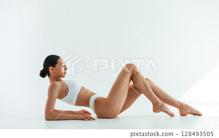 Side view, lying down. Young woman with slim body type is in fitness clothes in the studio 128493505