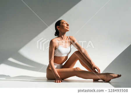 In the sunlight. Young woman with slim body type is in fitness clothes in the studio 128493508