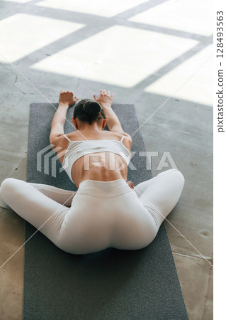 Using yoga mat for exercises. Young woman with slim body type is in fitness clothes in the studio Using yoga mat for exercises. Young woman with slim body type is in fitness clothes in the studio 128493563