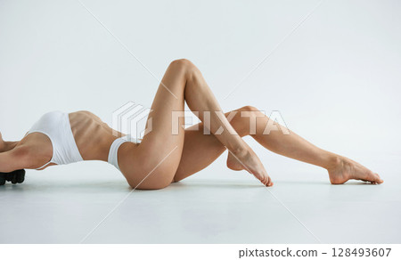 Side view, lying down. Young woman with slim body type is in fitness clothes in the studio Side view, lying down. Young woman with slim body type is in fitness clothes in the studio 128493607