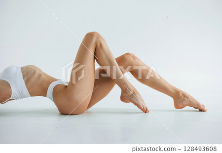 Side view, lying down. Young woman with slim body type is in fitness clothes in the studio 128493608