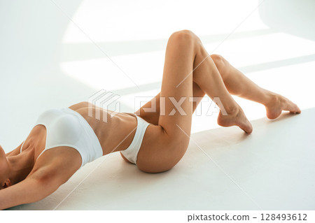 Straightens the back up, sitting on the floor. Young woman with slim body type is in fitness clothes in the studio 128493612