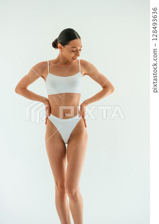 Front view. Young woman with slim body type is in fitness clothes in the studio Front view. Young woman with slim body type is in fitness clothes in the studio 128493636