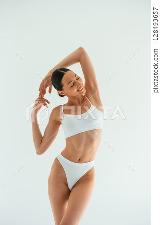 Hands behind the neck and up. Young woman with slim body type is in fitness clothes in the studio 128493657