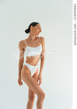 Relaxed, standing against white background. Young woman with slim body type is in fitness clothes in the studio Relaxed, standing against white background. Young woman with slim body type is in fitness clothes in the studio 128493661