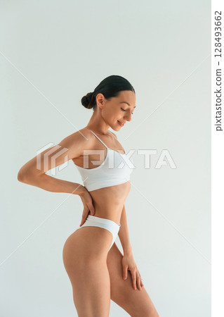 Relaxed, standing against white background. Young woman with slim body type is in fitness clothes in the studio Relaxed, standing against white background. Young woman with slim body type is in fitness clothes in the studio 128493662