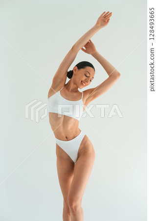 Raising hands up. Young woman with slim body type is in fitness clothes in the studio 128493665