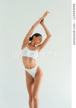 Raising hands up. Young woman with slim body type is in fitness clothes in the studio Raising hands up. Young woman with slim body type is in fitness clothes in the studio 128493666