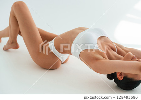 Stretching on the floor, close up view. Young woman with slim body type is in fitness clothes in the studio Stretching on the floor, close up view. Young woman with slim body type is in fitness clothes in the studio 128493680